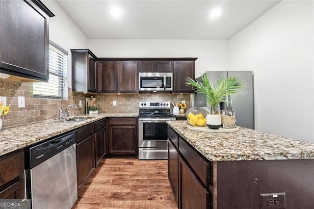 kitchen with wood finished floors, a sink, a center island, dark brown cabinetry, and appliances with stainless steel finishes