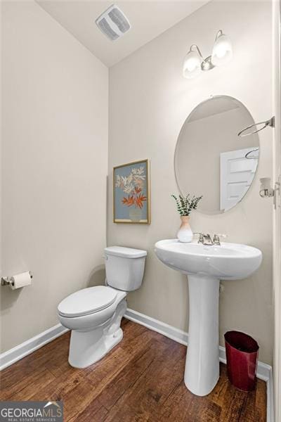 half bathroom featuring wood finished floors, visible vents, toilet, and baseboards