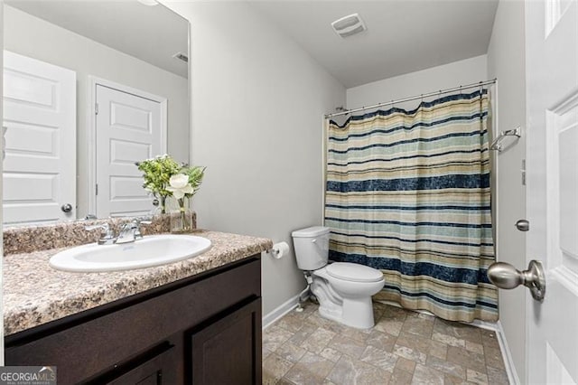bathroom featuring stone finish floor, visible vents, toilet, vanity, and baseboards
