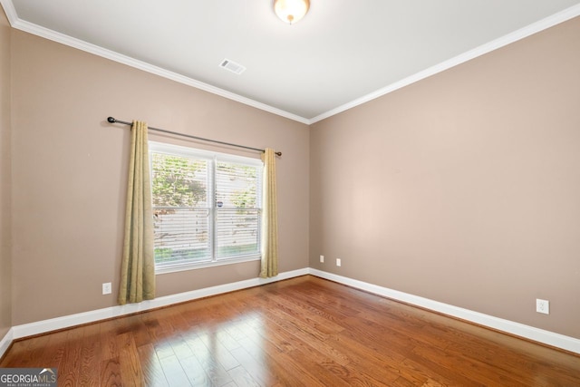 unfurnished room with wood finished floors, visible vents, baseboards, and ornamental molding