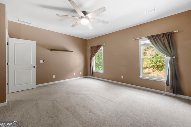 empty room with ceiling fan, carpet floors, visible vents, and a wealth of natural light