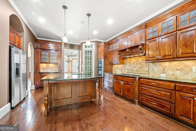 kitchen featuring crown molding, a sink, arched walkways, stainless steel appliances, and backsplash