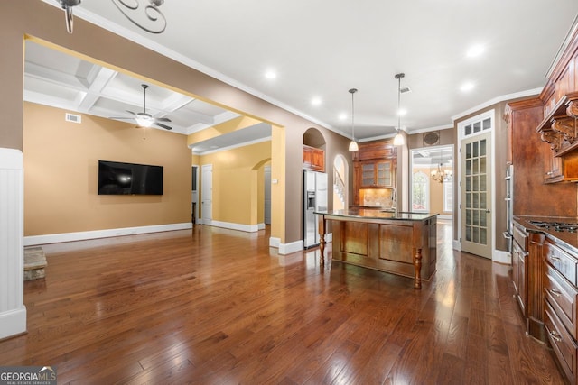 kitchen featuring a kitchen island with sink, arched walkways, dark countertops, a kitchen bar, and stainless steel refrigerator with ice dispenser