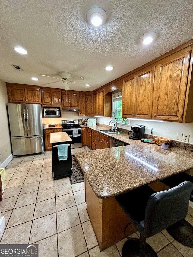 2118 Deer Run Cir, Tifton, GA 31793 - kitchen with appliances with stainless steel finishes, a sink, brown cabinets, a peninsula, and light stone countertops