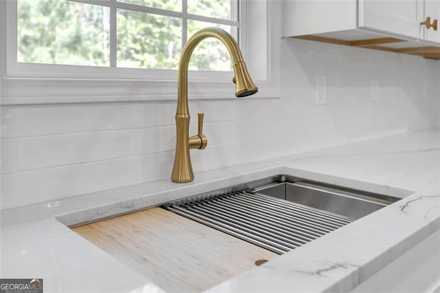 room details featuring a sink, white cabinetry, and light stone countertops