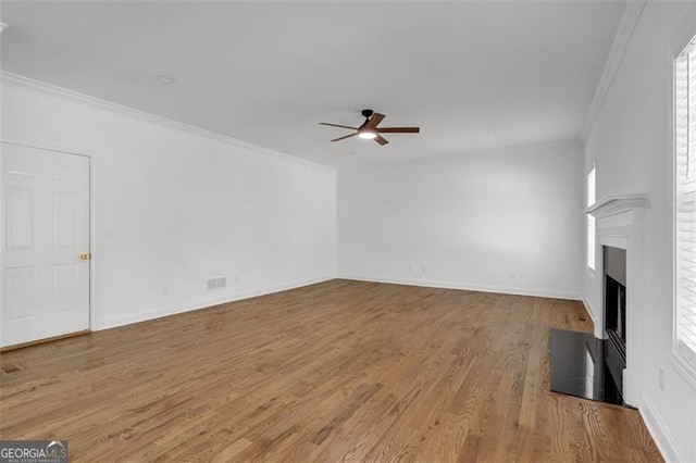 unfurnished living room with crown molding, wood finished floors, a fireplace, baseboards, and a ceiling fan