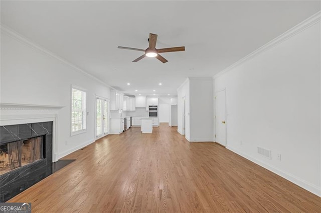 unfurnished living room featuring crown molding, a fireplace, baseboards, light wood-type flooring, and a ceiling fan