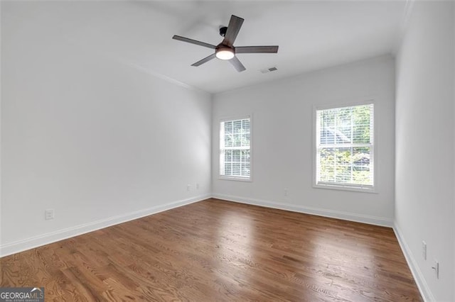 empty room featuring a healthy amount of sunlight, baseboards, wood finished floors, and visible vents