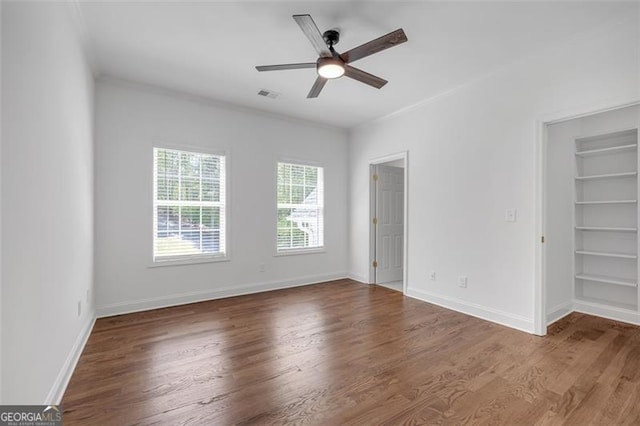 unfurnished bedroom with a walk in closet, baseboards, visible vents, and wood finished floors