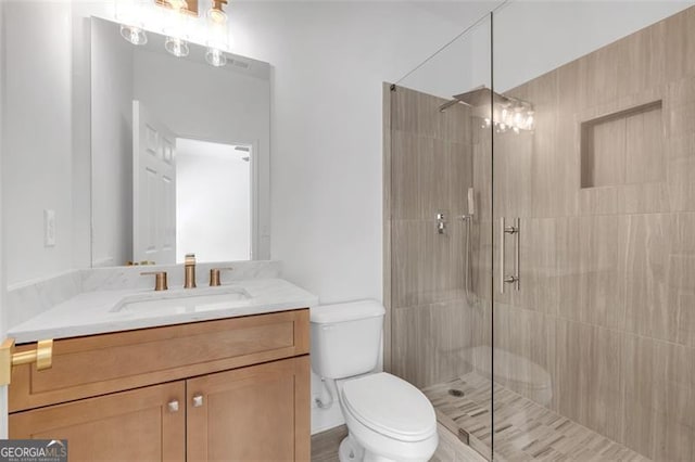 bathroom featuring vanity, a tile shower, and toilet