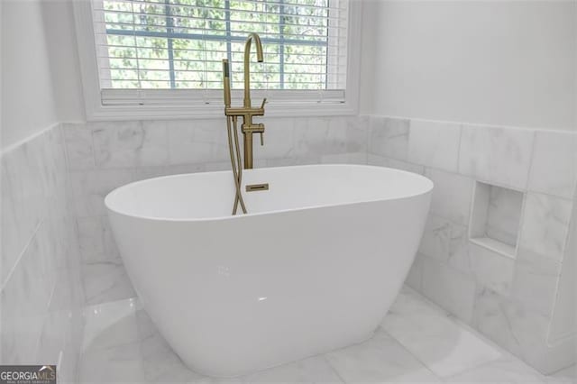 bathroom with tile walls, a soaking tub, wainscoting, and marble finish floor