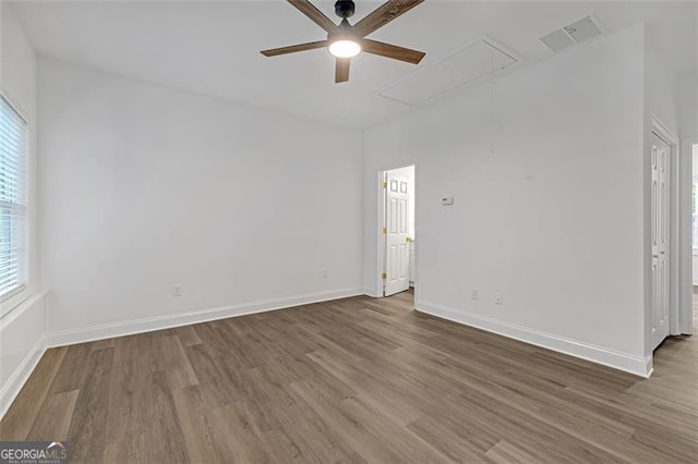 empty room with visible vents, wood finished floors, a healthy amount of sunlight, attic access, and ceiling fan