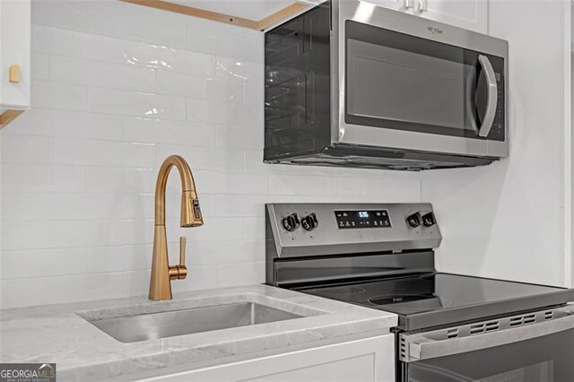 kitchen with decorative backsplash, a sink, light stone counters, stainless steel appliances, and white cabinetry