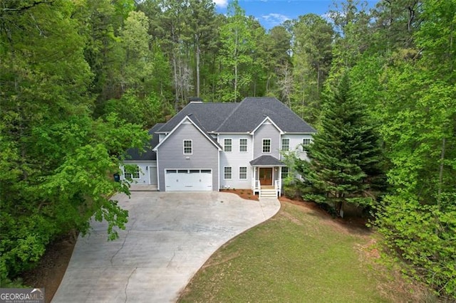 colonial inspired home featuring a garage, a view of trees, concrete driveway, and a front yard