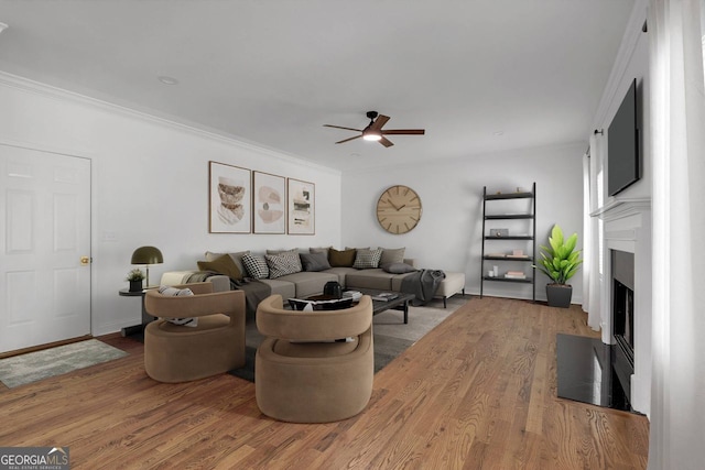 living room with crown molding, a fireplace with flush hearth, light wood-style flooring, and ceiling fan