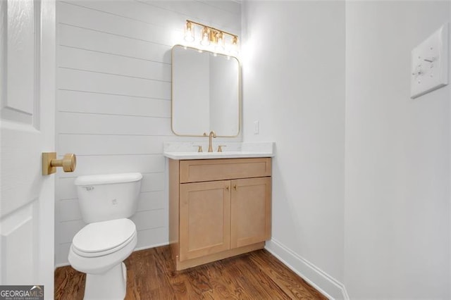 half bathroom with vanity, baseboards, toilet, and wood finished floors