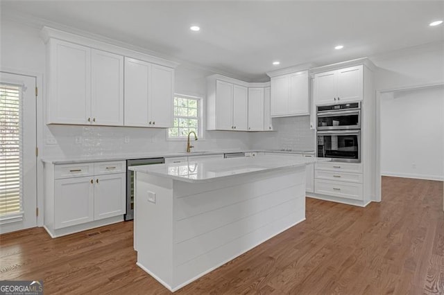 kitchen featuring white cabinets, appliances with stainless steel finishes, a sink, light countertops, and backsplash