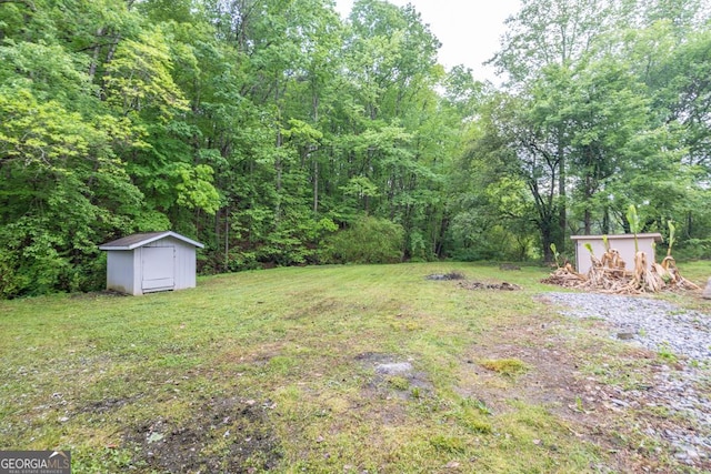 view of yard featuring a shed, a forest view, and an outbuilding