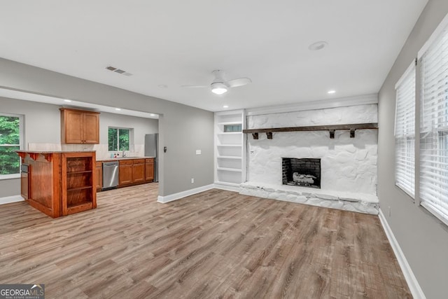 unfurnished living room with a fireplace, a sink, baseboards, and light wood-style floors