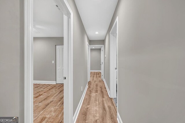 hall featuring baseboards, light wood-type flooring, and recessed lighting