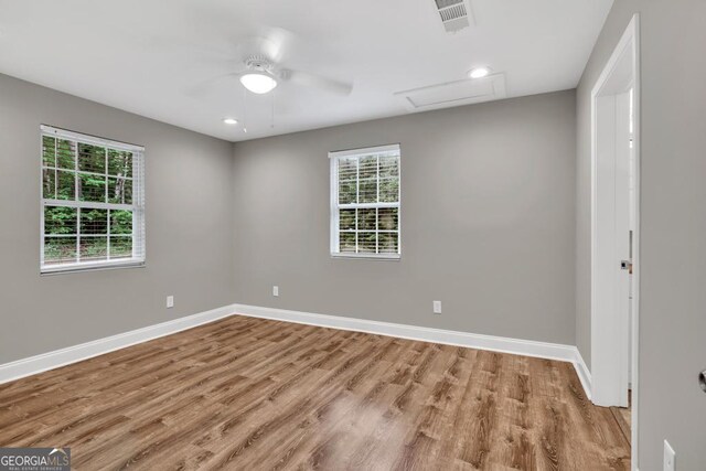 empty room with visible vents, attic access, a healthy amount of sunlight, and wood finished floors