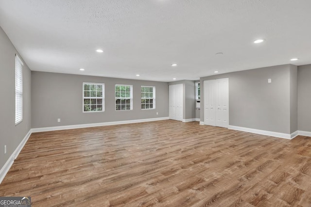unfurnished living room featuring a textured ceiling, wood finished floors, recessed lighting, and baseboards
