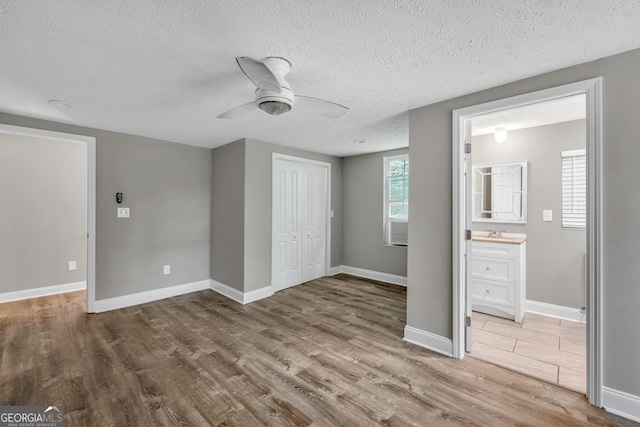 unfurnished bedroom with a textured ceiling, a sink, baseboards, a closet, and wood finished floors