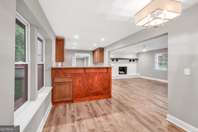 kitchen featuring recessed lighting, brown cabinets, a fireplace with raised hearth, light wood-style flooring, and baseboards