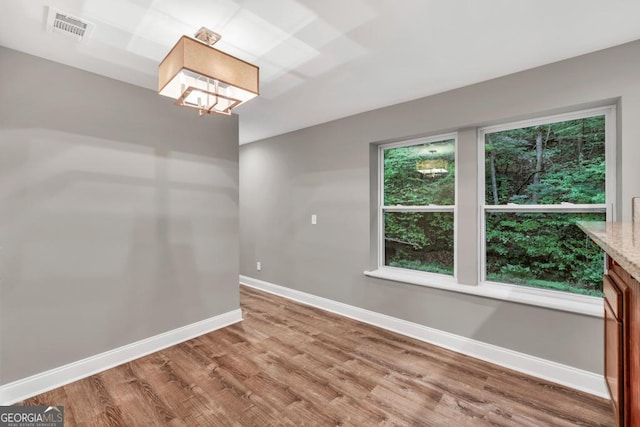 unfurnished room with baseboards, light wood-type flooring, visible vents, and an inviting chandelier