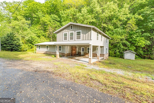 view of front of house featuring an outdoor structure, board and batten siding, a shed, covered porch, and a forest view