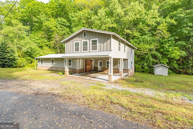 view of front of house with board and batten siding, a porch, a wooded view, a storage unit, and an outbuilding