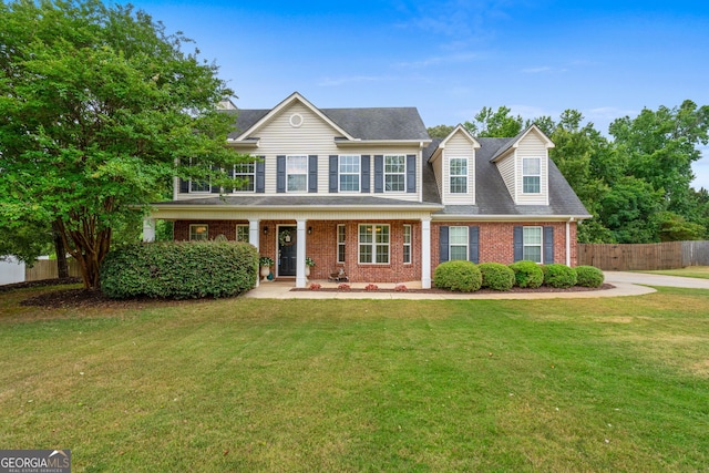view of front facade featuring covered porch, fence, brick siding, a shingled roof, and a front yard