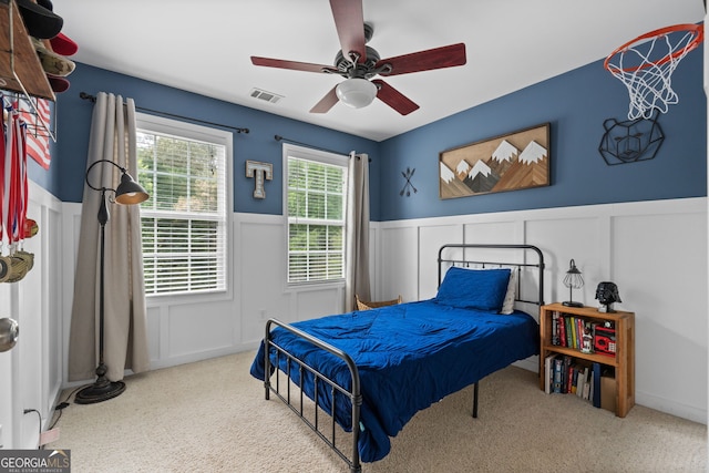 bedroom featuring a decorative wall, carpet floors, visible vents, and wainscoting