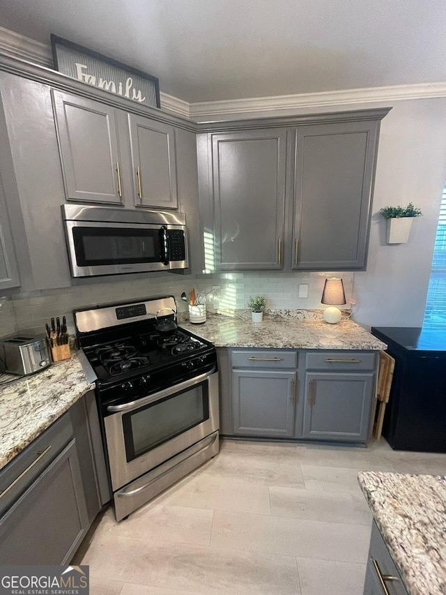 kitchen with gray cabinetry, crown molding, backsplash, and stainless steel appliances