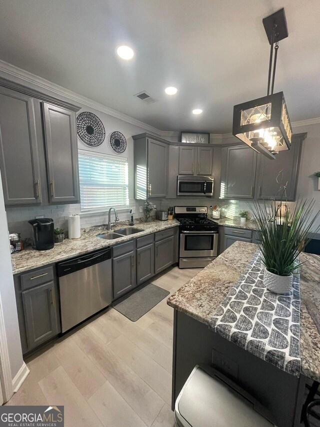 kitchen with a sink, light wood-style flooring, stainless steel appliances, visible vents, and ornamental molding