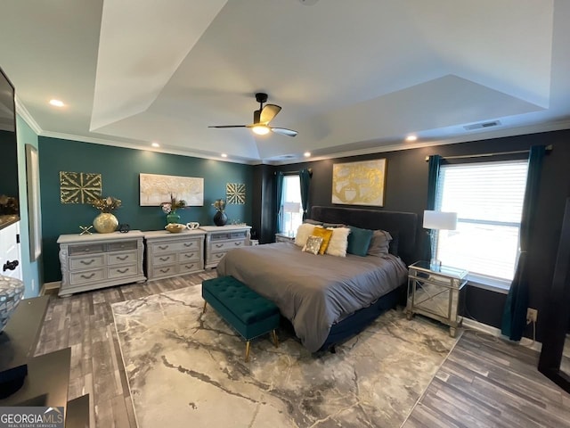 bedroom featuring visible vents, ornamental molding, wood finished floors, ceiling fan, and a raised ceiling