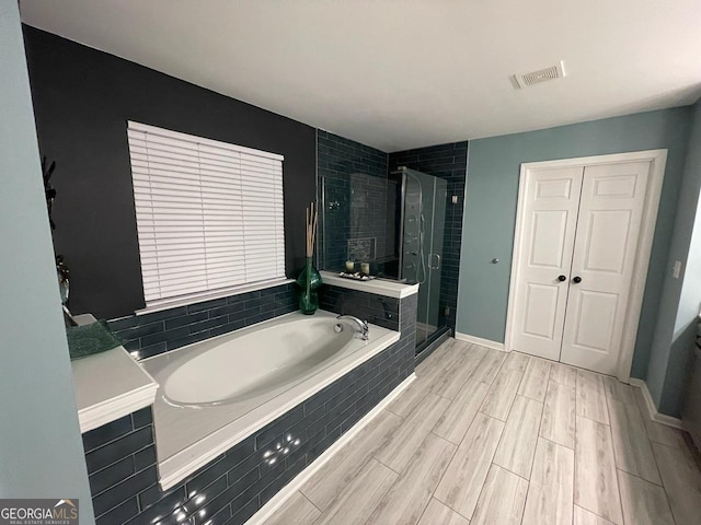 full bath featuring visible vents, a garden tub, wood finished floors, baseboards, and a stall shower