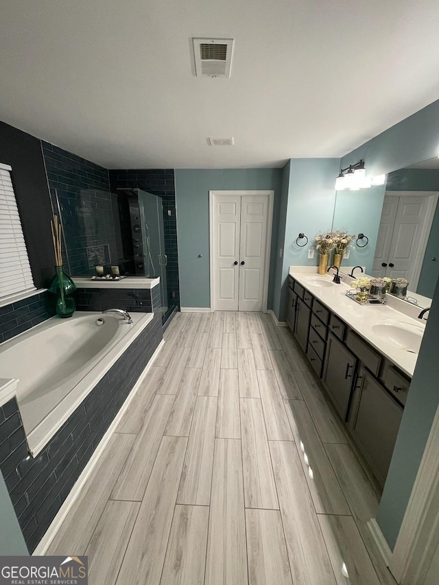 bathroom with visible vents, a garden tub, wood finished floors, a shower stall, and a sink