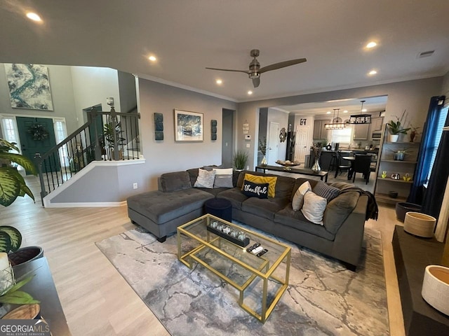 living room with ceiling fan, light wood-style floors, recessed lighting, ornamental molding, and stairway