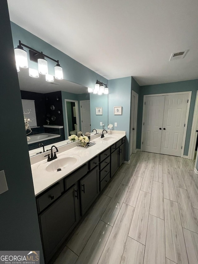 full bath featuring a sink, wood finish floors, double vanity, and visible vents