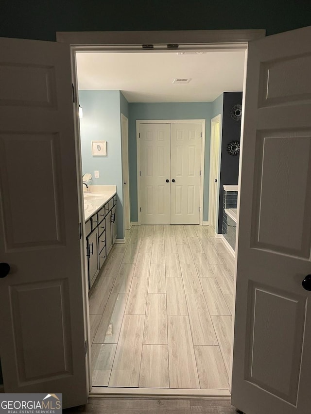 hallway featuring baseboards, visible vents, a sink, and light wood-type flooring