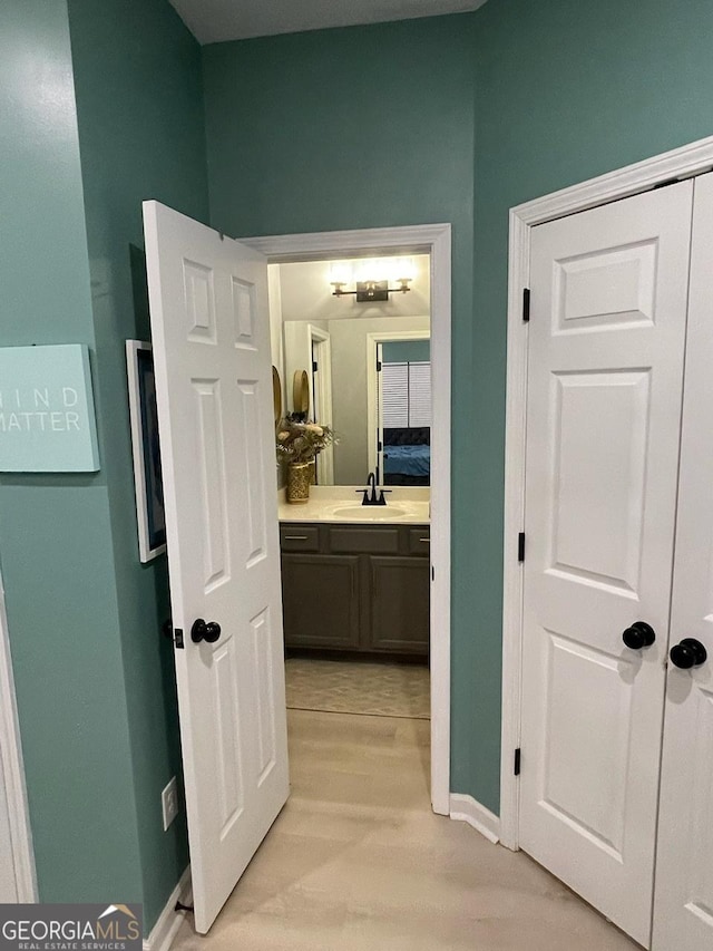 hallway with baseboards, a sink, and light wood-style flooring
