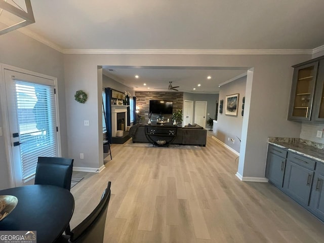 living room with crown molding, ceiling fan, a fireplace, baseboards, and light wood-type flooring