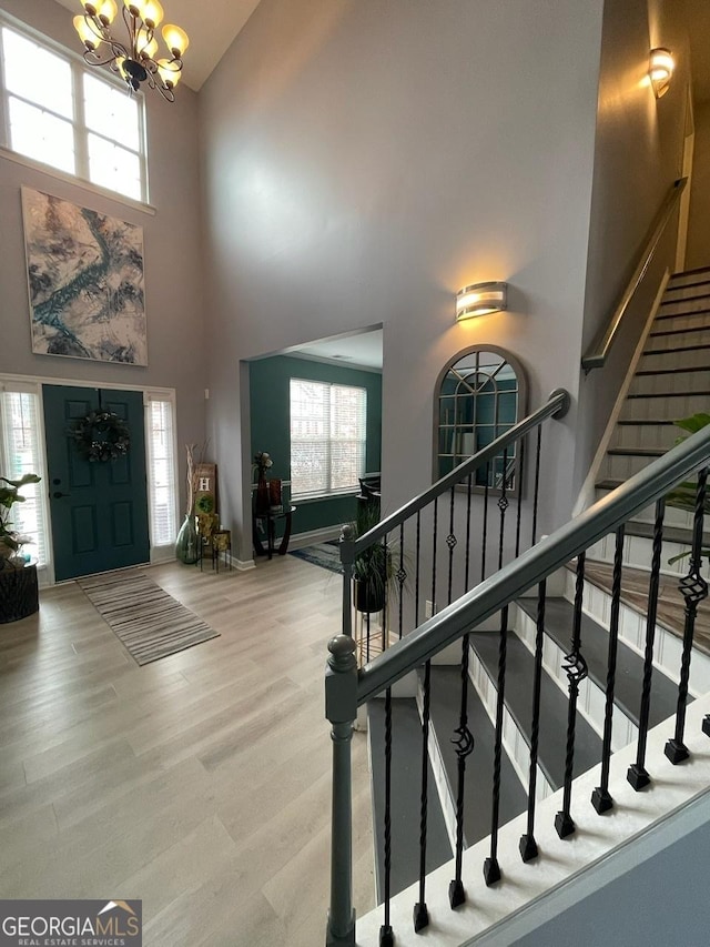 entrance foyer with a notable chandelier, high vaulted ceiling, baseboards, wood finished floors, and stairway