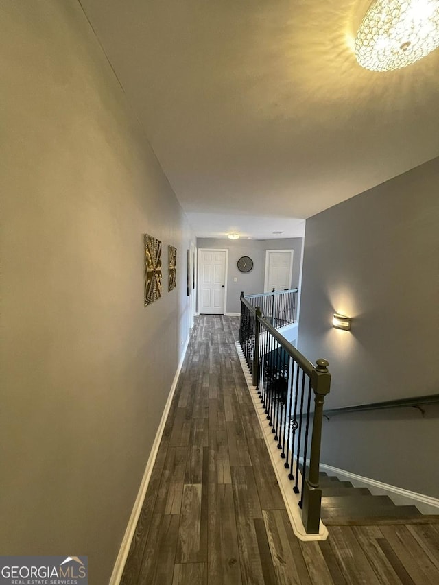 hallway with baseboards, a notable chandelier, dark wood-style flooring, and an upstairs landing