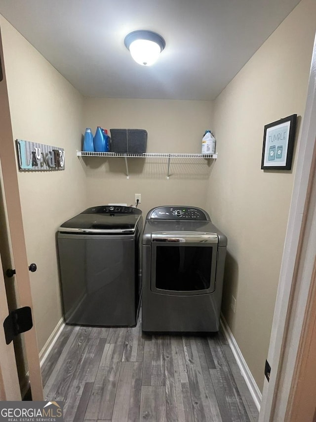 clothes washing area with laundry area, baseboards, wood finished floors, and separate washer and dryer