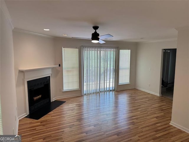unfurnished living room with crown molding, wood finished floors, a ceiling fan, a fireplace with flush hearth, and baseboards
