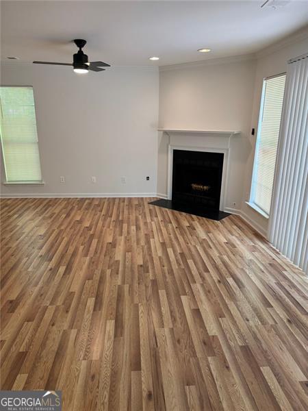 unfurnished living room with ornamental molding, wood finished floors, a fireplace with flush hearth, ceiling fan, and baseboards