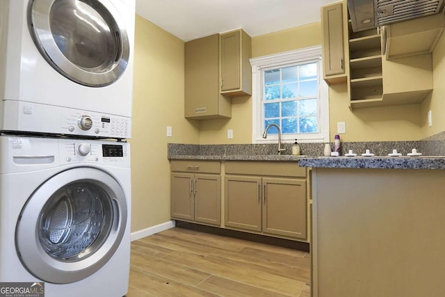 laundry area featuring light wood finished floors, a sink, baseboards, stacked washer and clothes dryer, and cabinet space