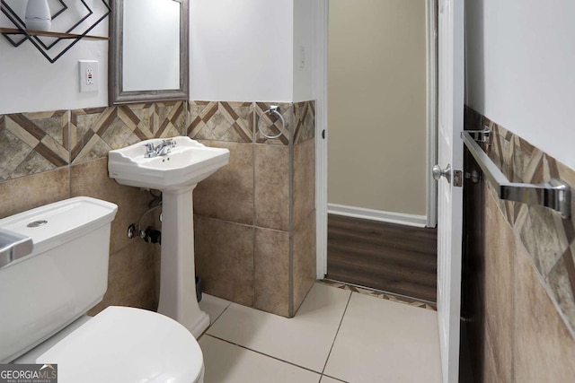 half bathroom featuring tile patterned flooring, tile walls, toilet, and a wainscoted wall